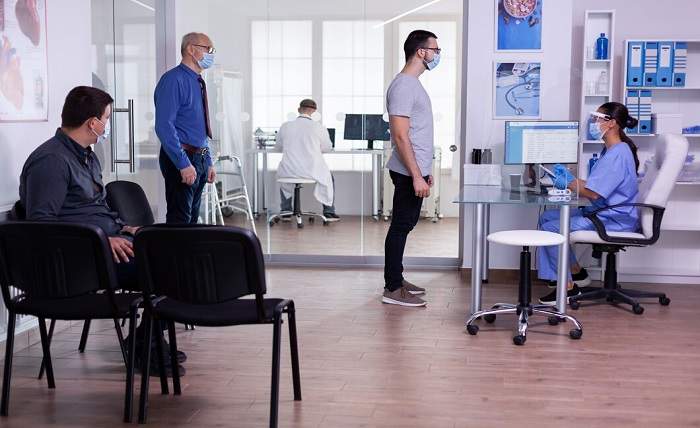 young man checking appointment respecting social distancing hospital waiting room nurse looking computer wearing face mask against covid 19 482257 2003